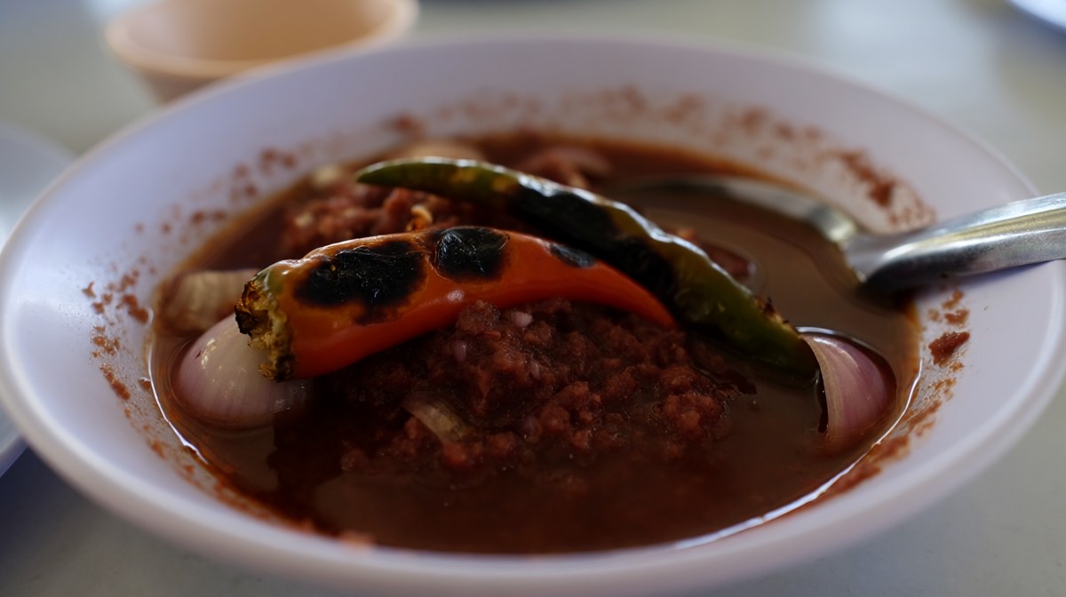 A bowl of dark nam prik pao with visible shrimp paste flecks, charred chilli skin and shallot pieces