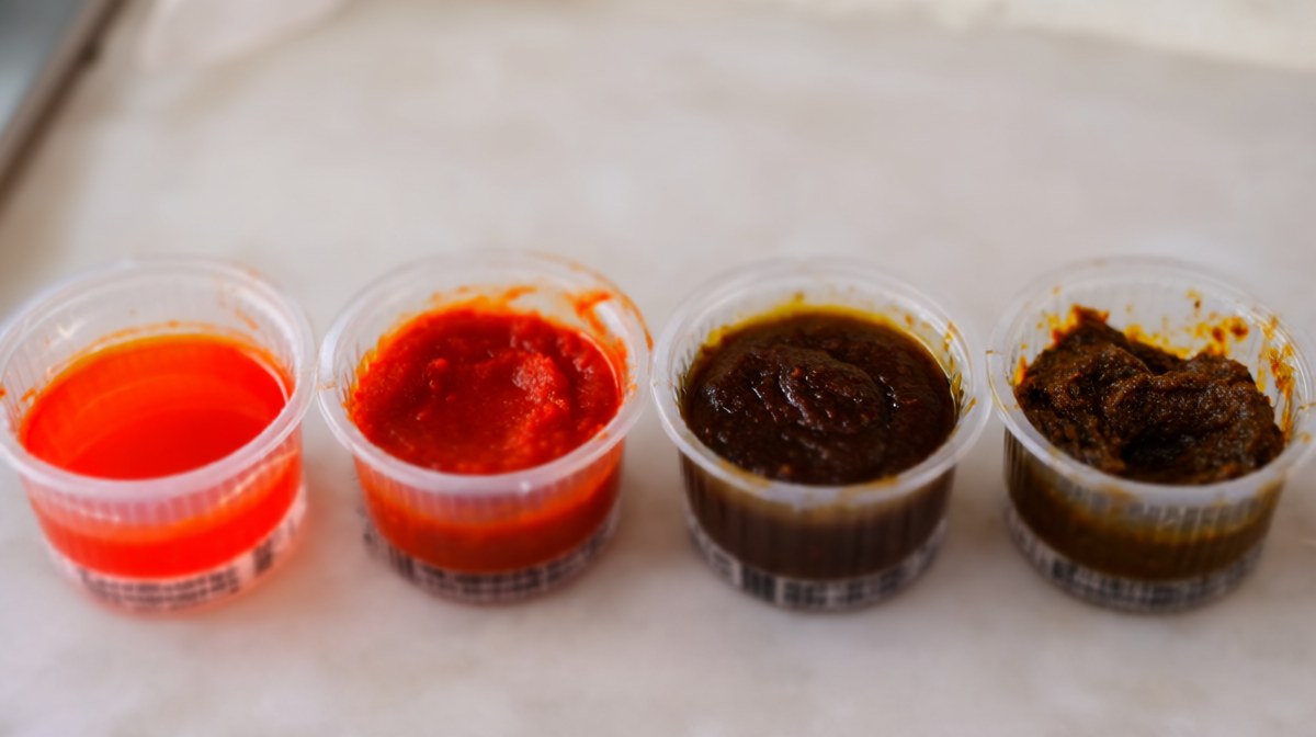 Four bowls in a row of chilli pastes from bright thin red through to dark thick brown