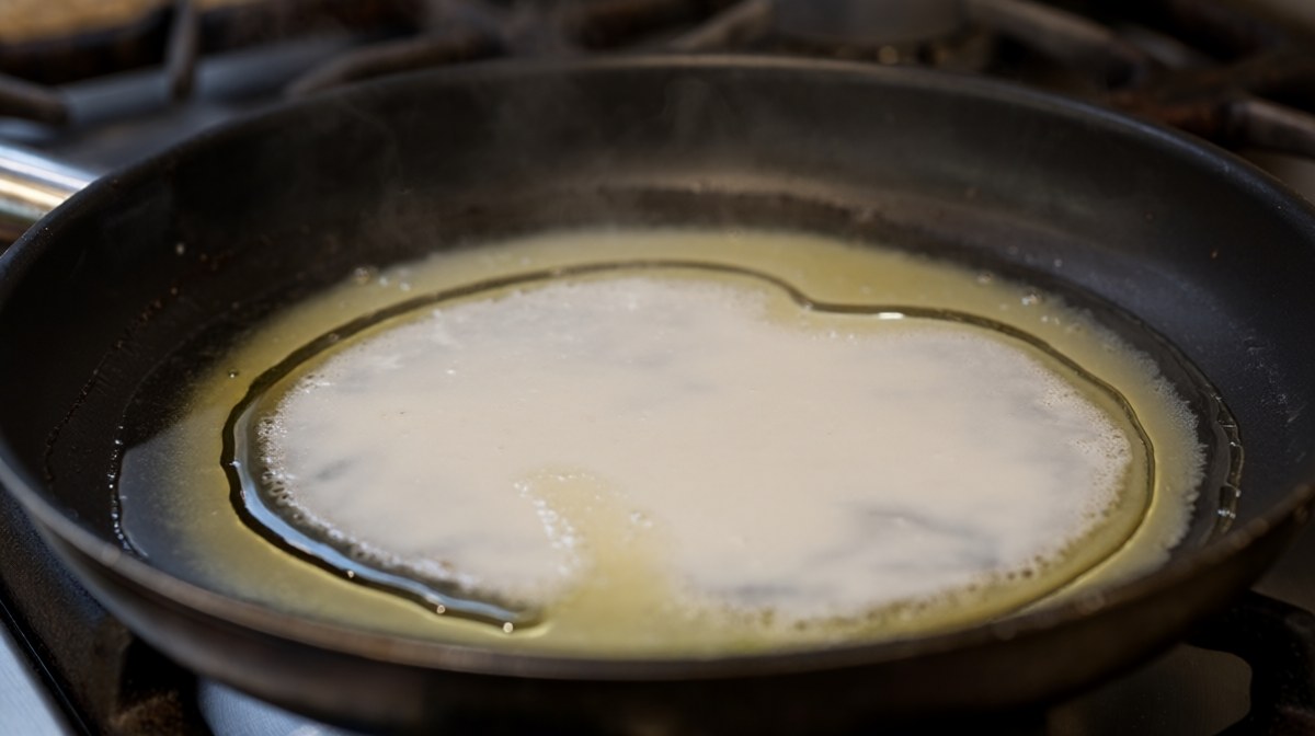 A pan of coconut milk reducing with thicker cream rising and a ring of clear oil around the edge
