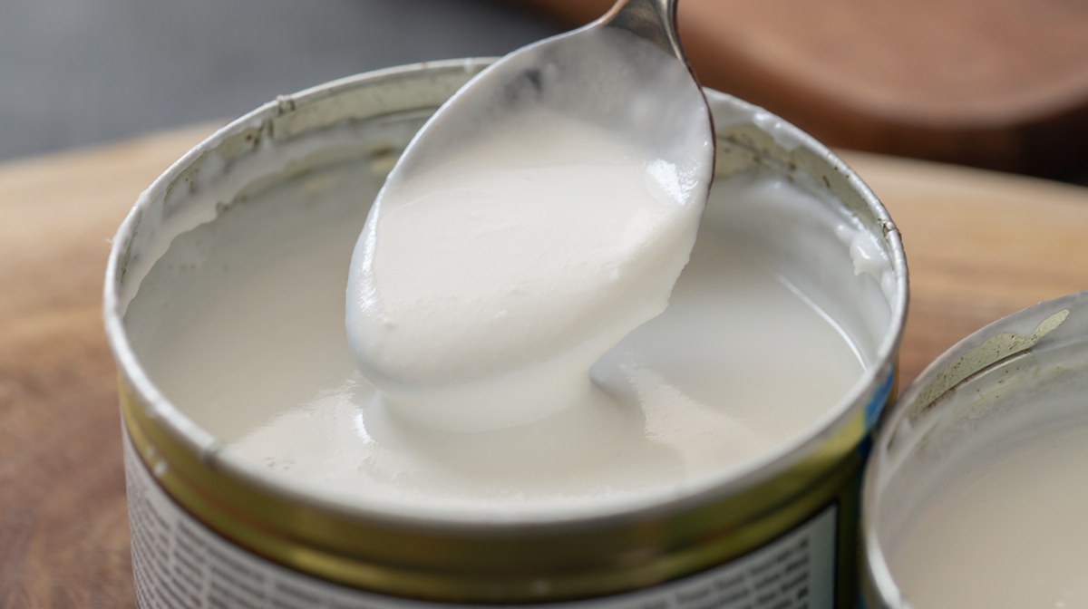 An open tin of coconut milk with thick cream sitting on top, a spoon lifting a heavy scoop of the cream