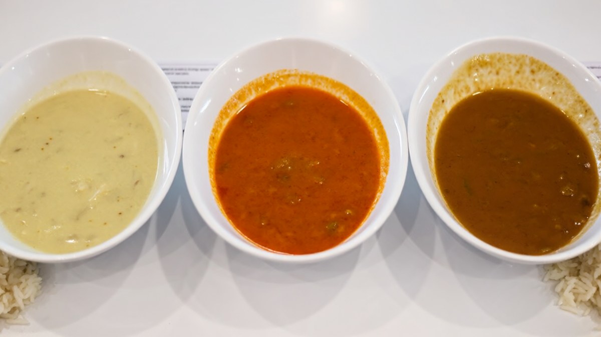 Three bowls of curry side by side, pale yellow, deep orange red and rich brown, each with rice